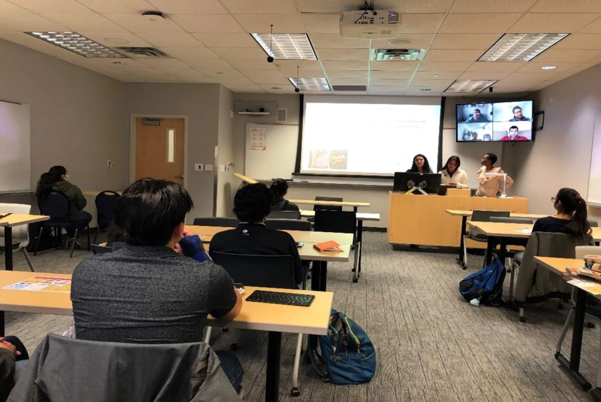 Students in a classroom watching a lecture with remote participants on screen